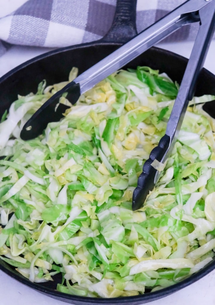 Sautéing cabbage in a cast iron skillet with tongs.  