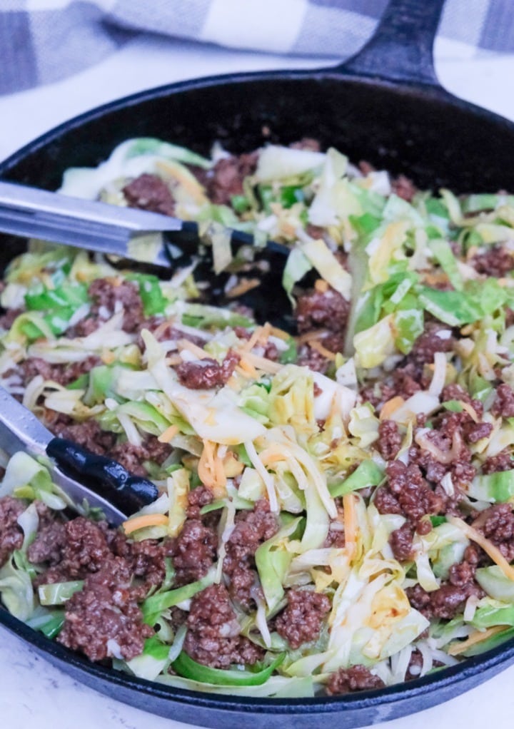 Mixing cabbage and cheese with ground beef in a cast iron skillet. 