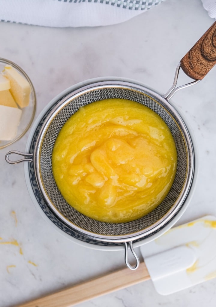 Straining lemon curd over a small bowl. 