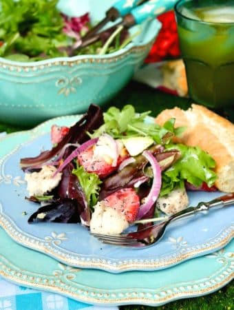 A light blue plate with strawberry avocado chicken salad on a blue napkin