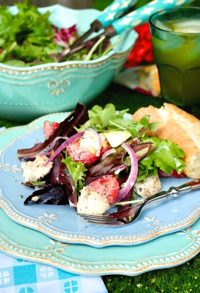 A light blue plate with strawberry avocado chicken salad on a blue napkin