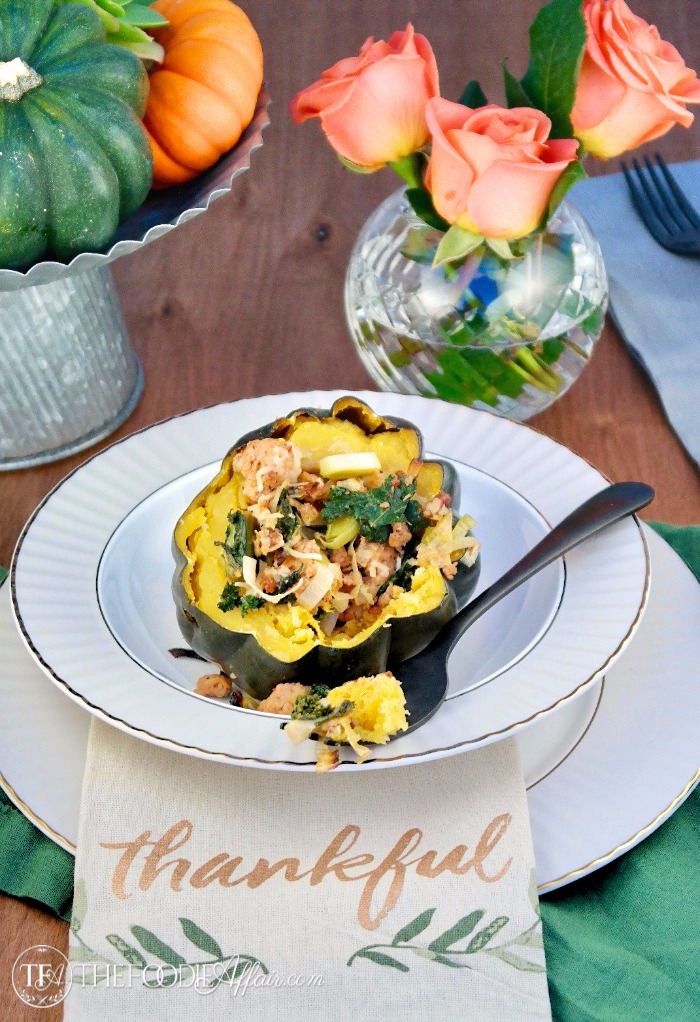 sausage stuffed acorn squash on a gray and white bowl with roses in the background 