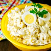 Low Carb potato salad made with cauliflower florets in a yellow serving bowl topped with sliced eggs.