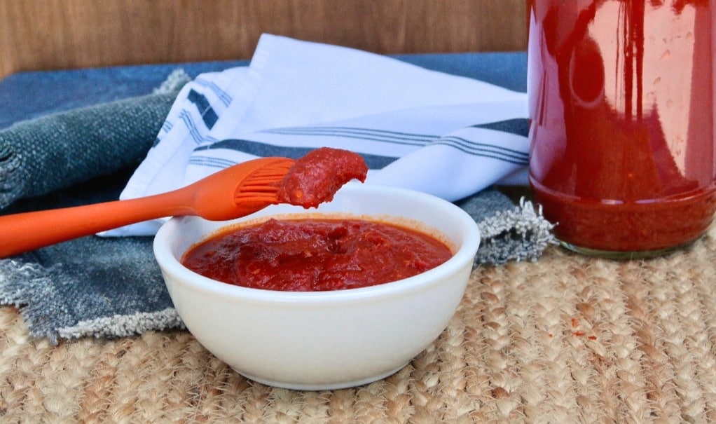 Homemade bbq sauce in a white bowl with a orange basting brush