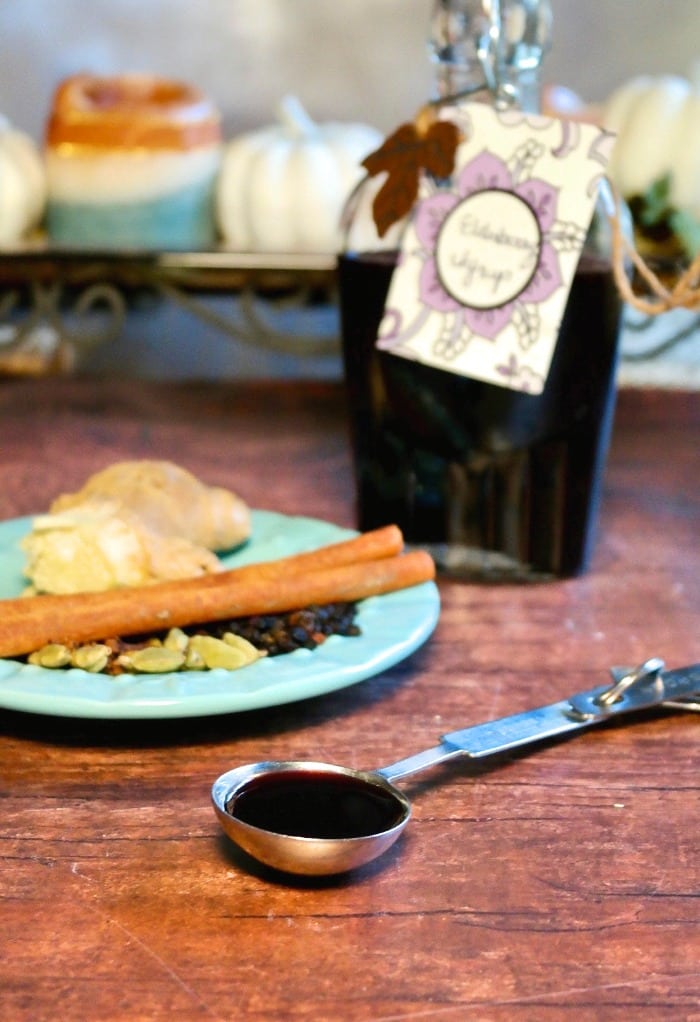Home made elderberry syrup recipe with a tablespoon of fresh syrup on a wood table 