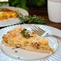 A slice of cheese and onion quiche topped with fresh thyme on a white and gray plate.