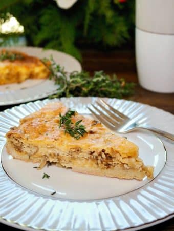 A slice of cheese and onion quiche topped with fresh thyme on a white and gray plate.