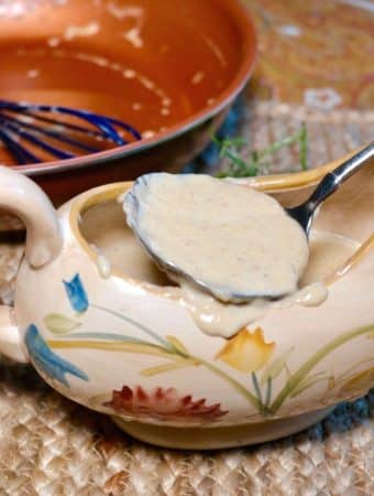 White low carb keto gravy in a gravy serving dish with a spoon scooping it out of the dish
