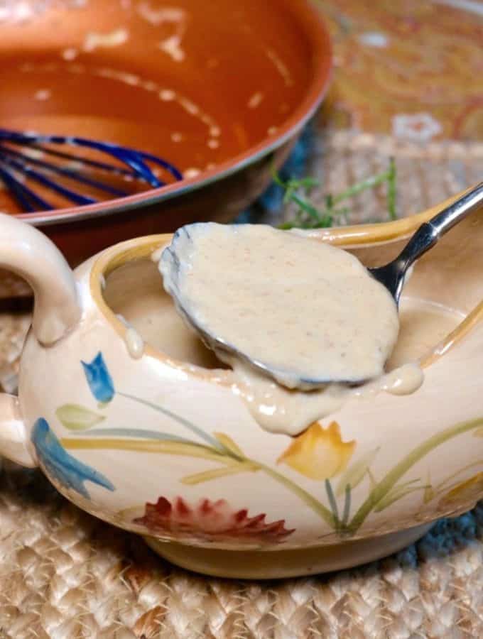 White low carb keto gravy in a gravy serving dish with a spoon scooping it out of the dish