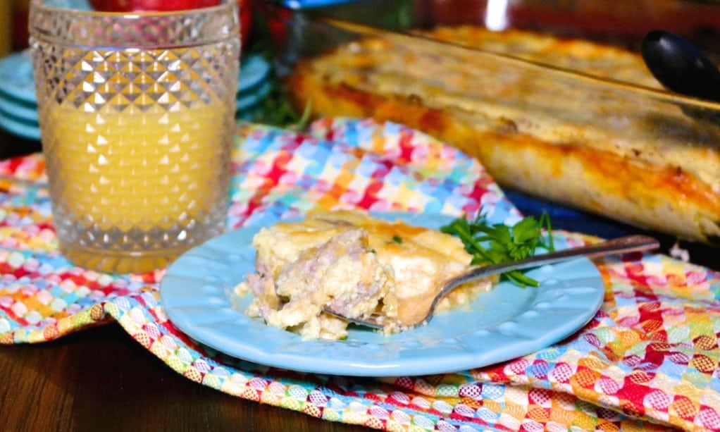 Slice of cheesy sausage casserole on a blue plate with a glass or orange juice on the side