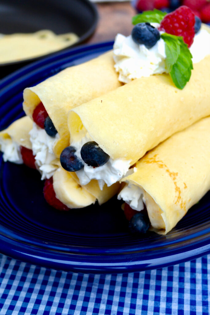 Fruit French crepes on a blue plate with whipped cream and berries.