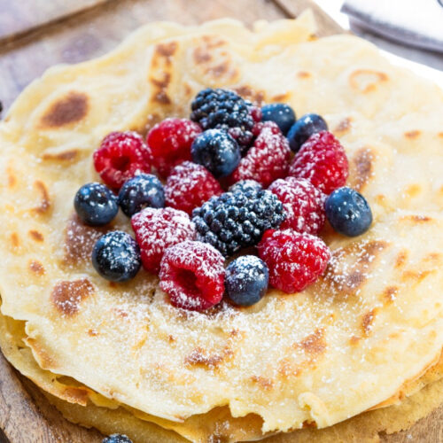 A stack of cooked crepes on a cutting board topped with fruit.