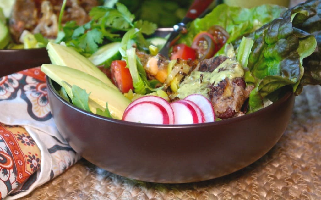 Brown bowl filled with salad, radish, and avocado slices