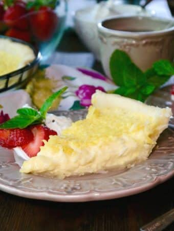 Slice of coconut custard pie on a tan plate with strawberries on the side