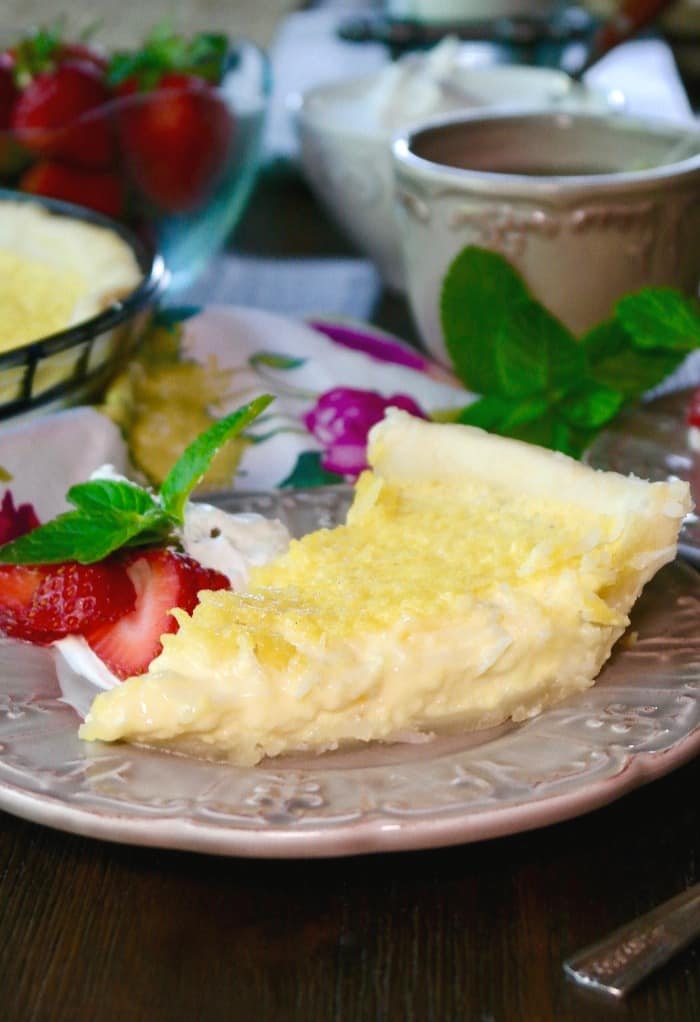 Slice of coconut custard pie on a tan plate with strawberries on the side