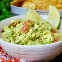 guacamole dip in a white bowl with slices of lime