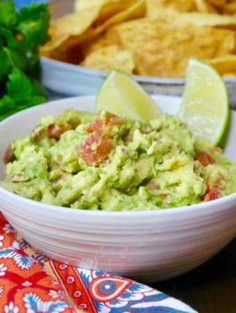 guacamole dip in a white bowl with slices of lime