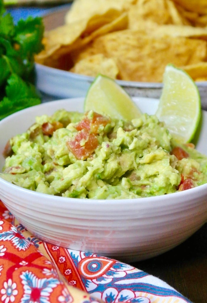 guacamole in a white bowl with slices of lime