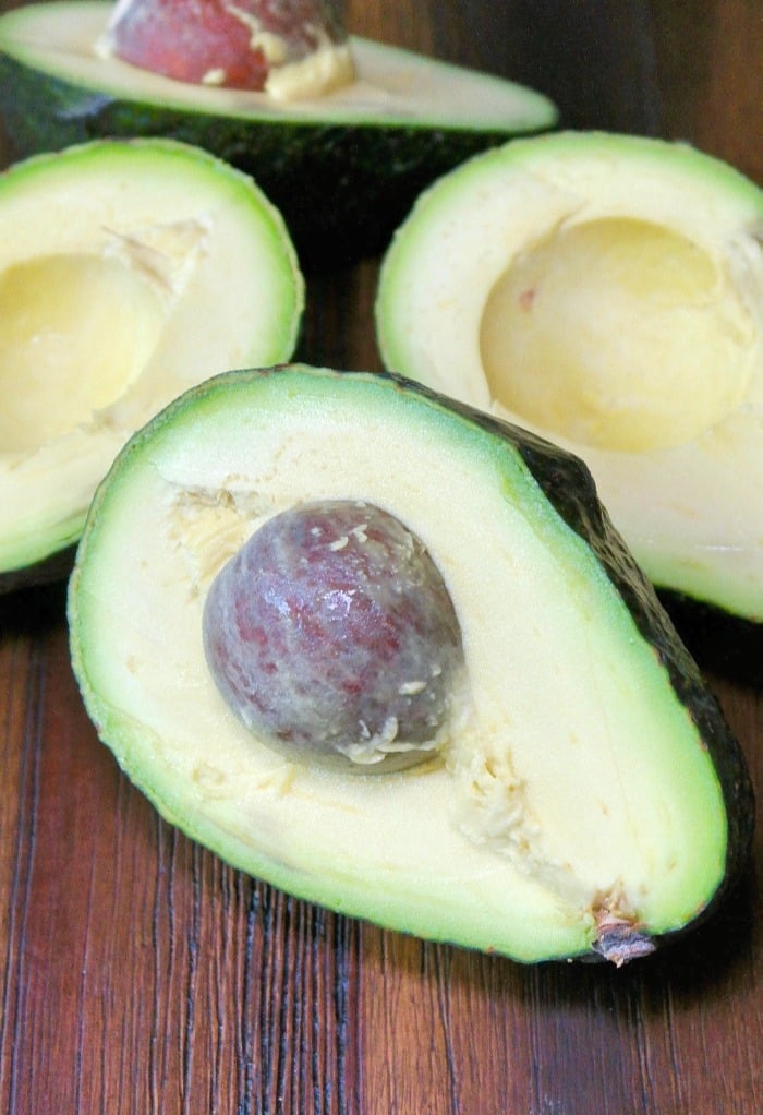 Fresh avocado sliced in half on a wooden plate