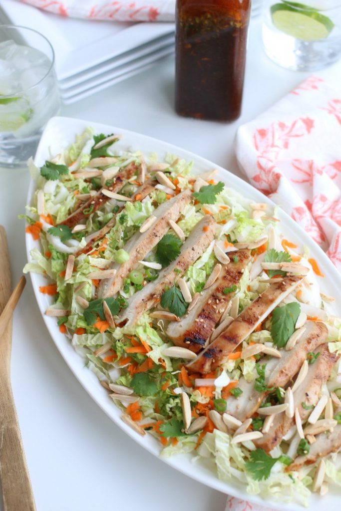 A grilled chicken salad recipe with cabbage, carrots and green onions. And a bottle of dressing on the side.