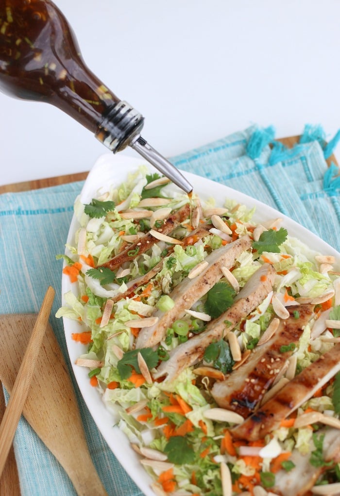 Pouring an Asian dressing on top of a grilled chicken salad.