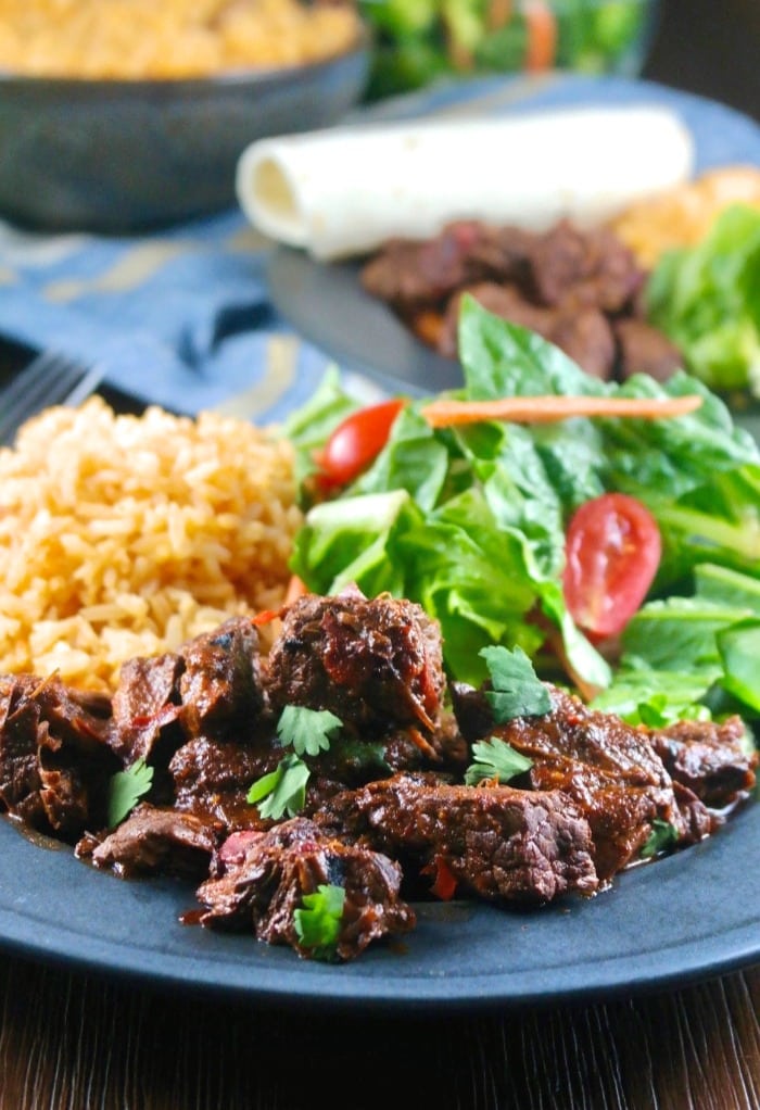 A black dinner plate filled with rice, salad and chili colorado con carne.