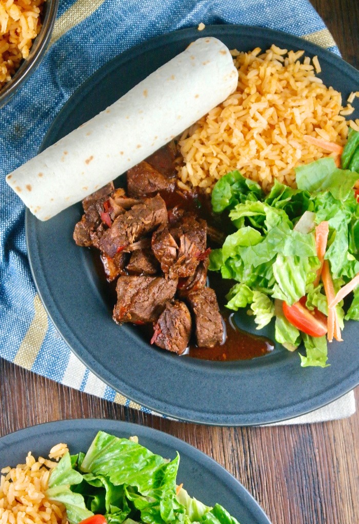 Chili colorado made in a pressure cooker on a black plate with rice and salad.