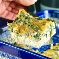 A slice of spinach egg bake in a blue casserole dish