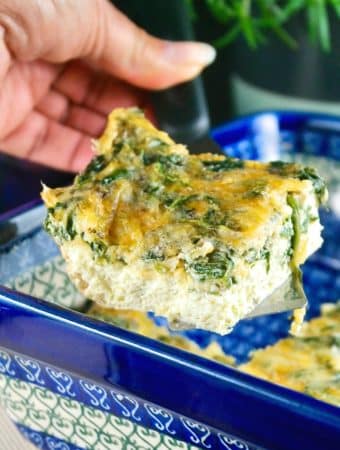 A slice of spinach egg bake in a blue casserole dish