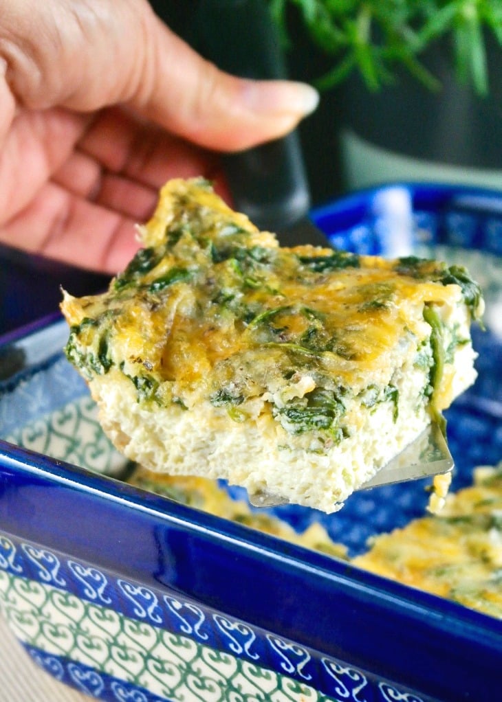 A slice of spinach egg bake in a blue casserole dish