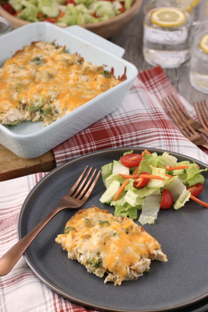 Low carb chicken casserole on a plate ready to eat with salad and the rest of the pan of keto chicken and broccoli in the background.