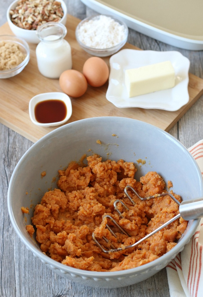 Mashed sweet potatoes in a bowl with more ingredients in the background for a sweet potato casserole.