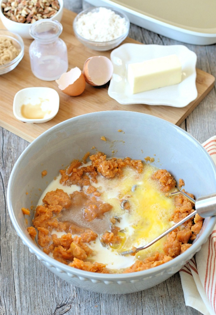 More ingredients for my sweet potato casserole recipe being added to the bowl with the masher.