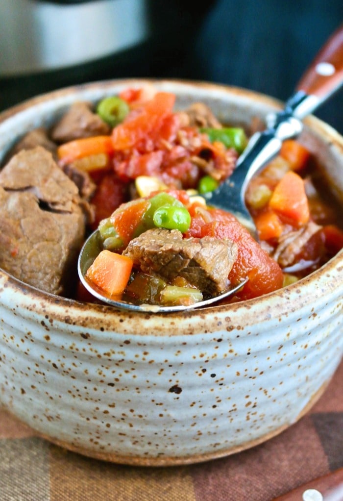 A bowl of beef vegetable soup wit a spoon digging in