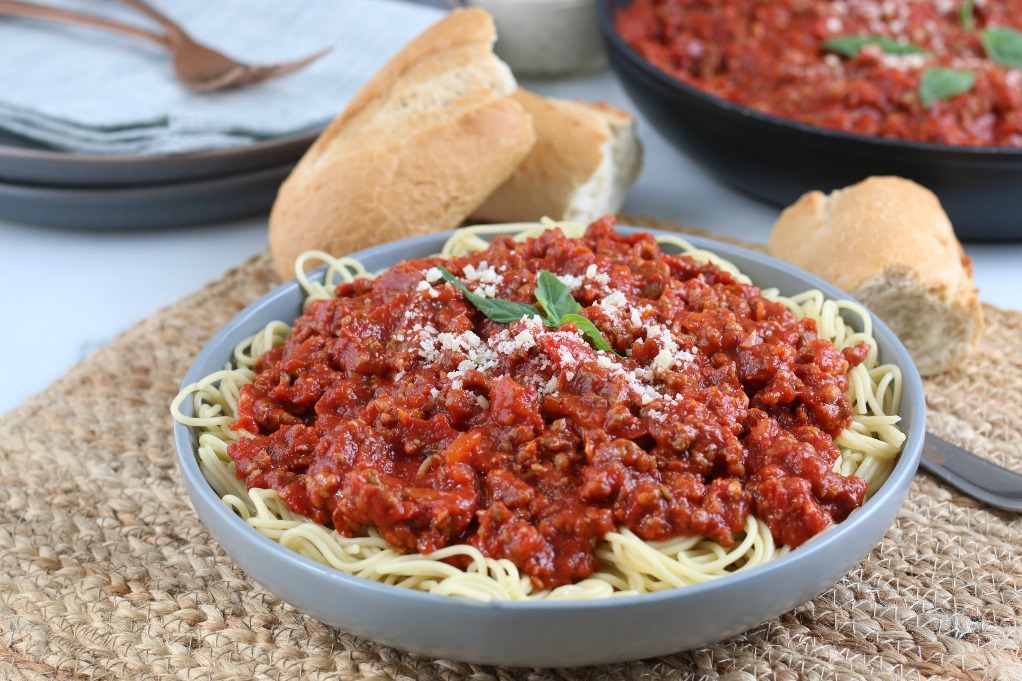 Here we see a horizontal view of a full dish of pasta with red meat sauce on top! 