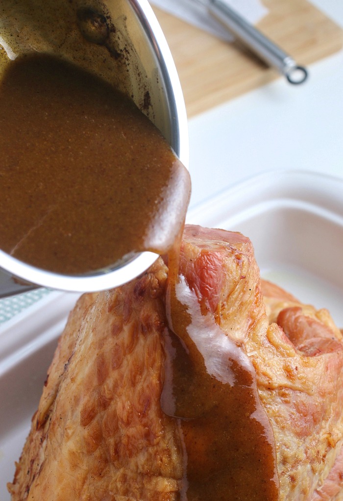 The quick ham glaze is being poured over the ham before it goes into the oven. 