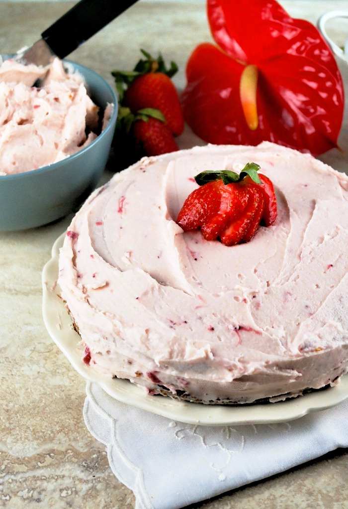 Sugar free cake topped with buttercream strawberry frosting on a white plate ready to be sliced. 