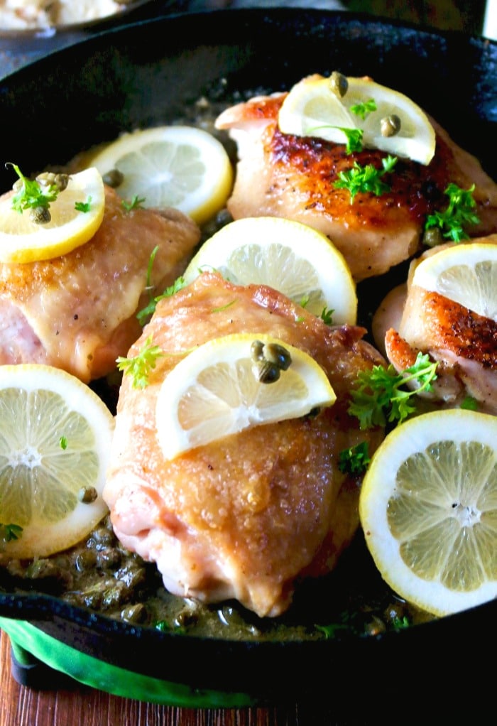 Iron skillet with chicken thighs and topped with lemon slices and capers