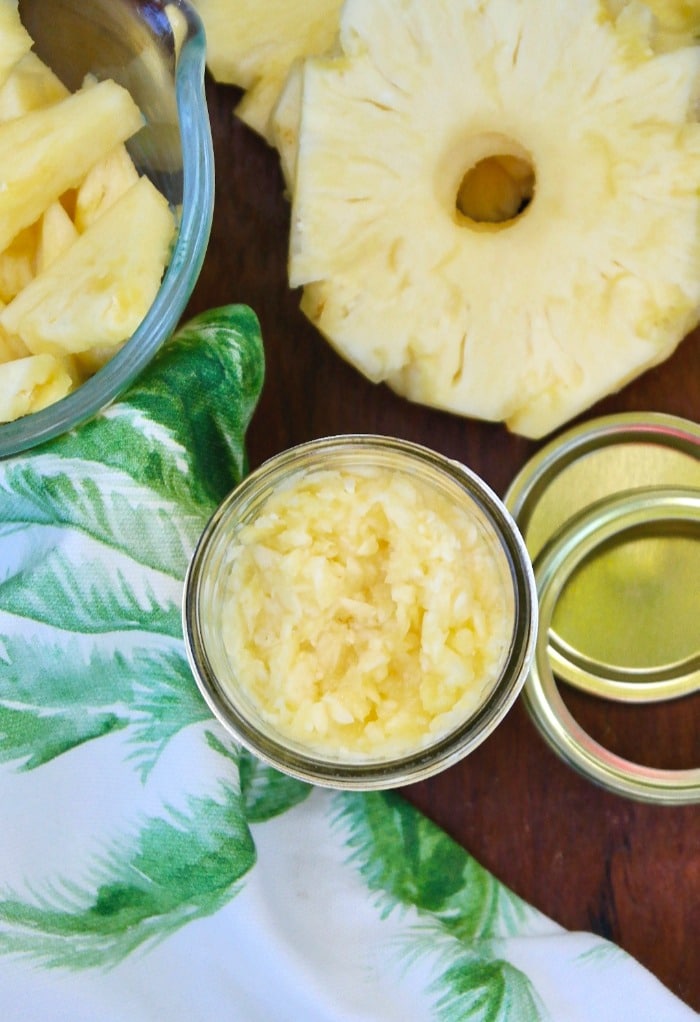 Top view of crushed pineapple in a jar with fresh pineapple slices on the side. 