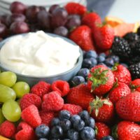 cream cheese fruit dip in a blue bowl surrounded with fresh fruit
