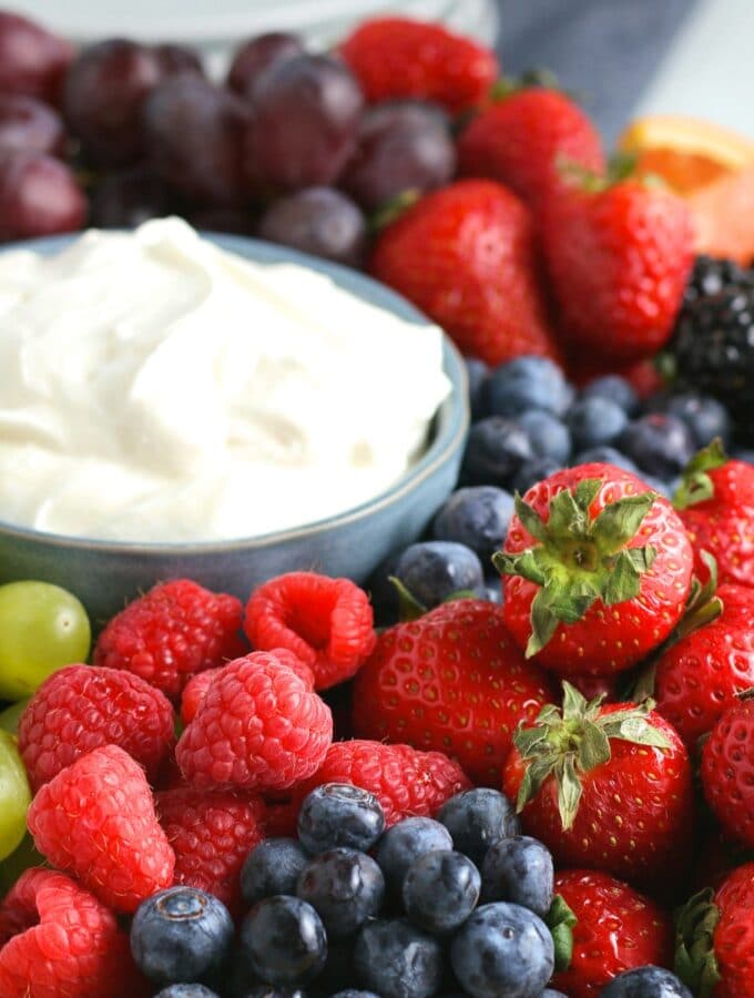 cream cheese fruit dip in a blue bowl surrounded with fresh fruit