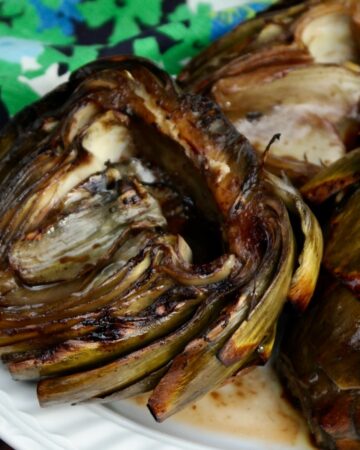 Grilled artichokes on a white serving plate.