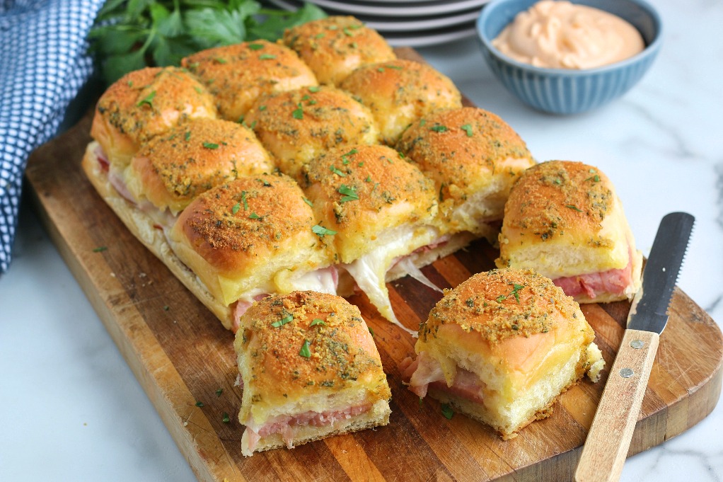 A horizontal view of the indulgent ham sliders on a cutting board ready to be shared and enjoyed. 