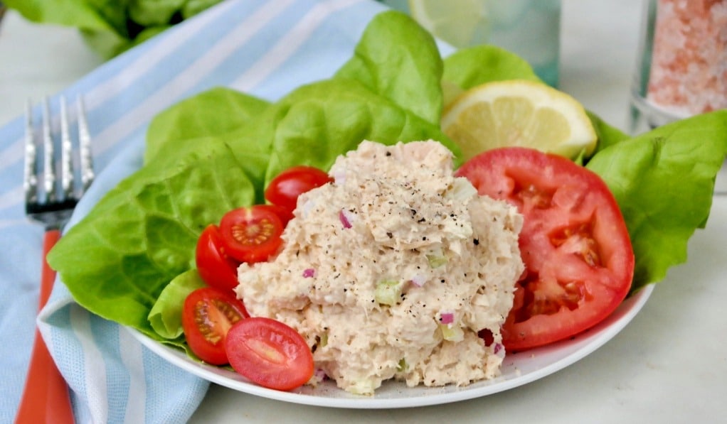 A scoop of low carb tuna salad on a white plate with lettuce and tomatoes. 