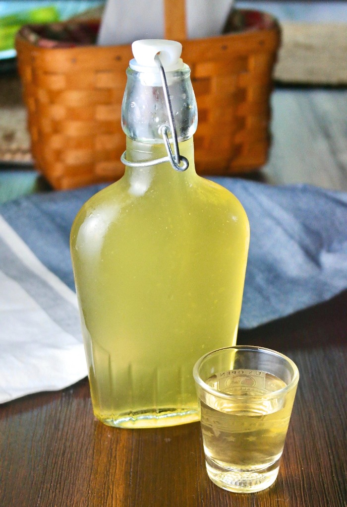 Homemade limoncello bottled and ready to be enjoyed with a shot glass on the side filled to the rim. 