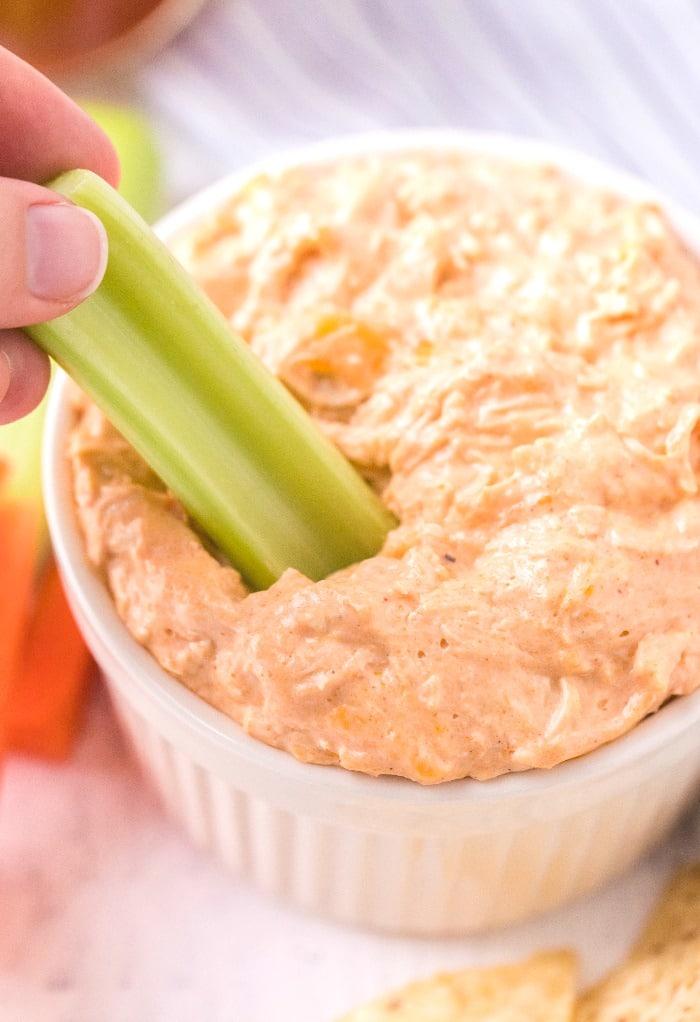 Keto buffalo chicken dip scooped in a small white bowl with celery stick ready to eat. 