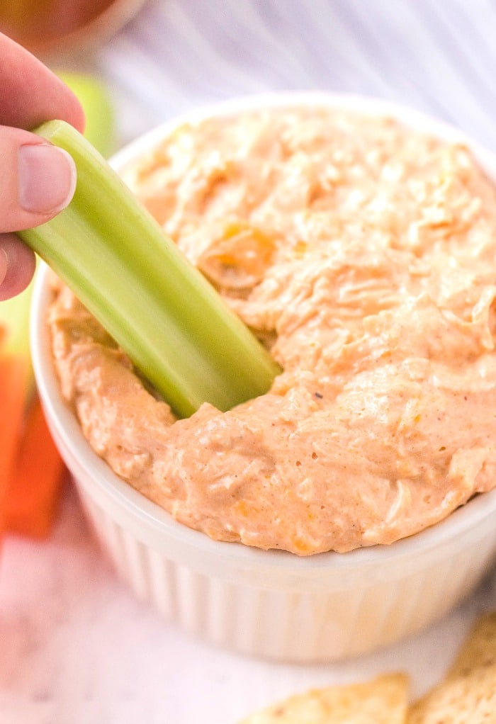 Keto buffalo chicken dip scooped in a small white bowl with celery stick ready to eat.