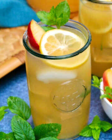 Peach lemonade in a clear glass with a slice of peach and lemon.