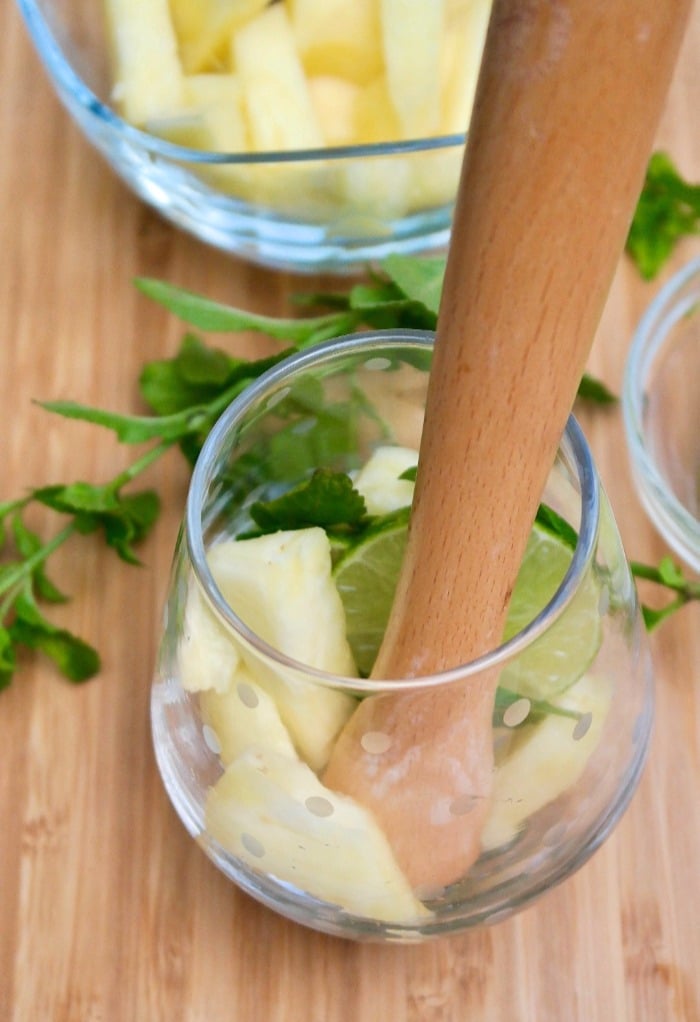 muddling pineapple and lime in a cocktail glass