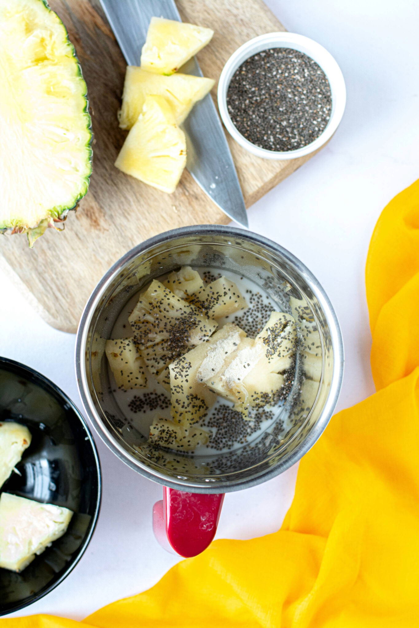 Ingredients for a pineapple smoothie in a blender with chia seeds before mixing.